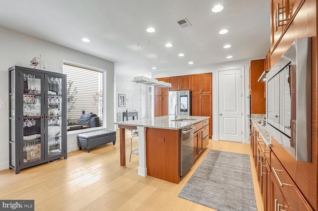 kitchen featuring appliances with stainless steel finishes, an island with sink, a kitchen breakfast bar, light stone counters, and light wood-type flooring