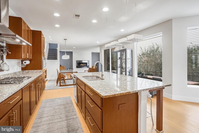 kitchen featuring extractor fan, decorative light fixtures, stainless steel gas stovetop, sink, and a kitchen island with sink