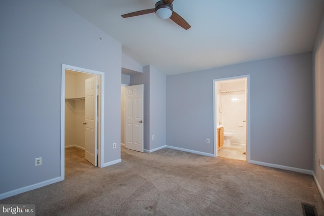 unfurnished bedroom featuring ensuite bath, vaulted ceiling, light carpet, a walk in closet, and a closet