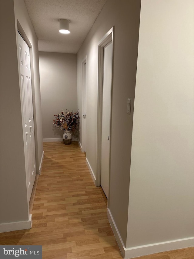 corridor with a textured ceiling and light wood-type flooring