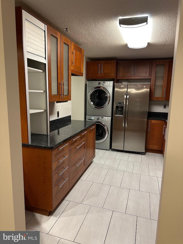 kitchen with stacked washer / dryer, stainless steel fridge, a textured ceiling, and dark stone counters