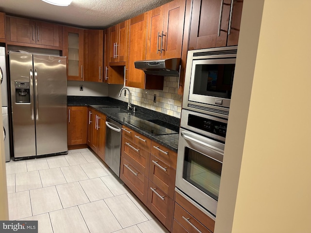 kitchen with sink, backsplash, stainless steel appliances, a textured ceiling, and dark stone counters