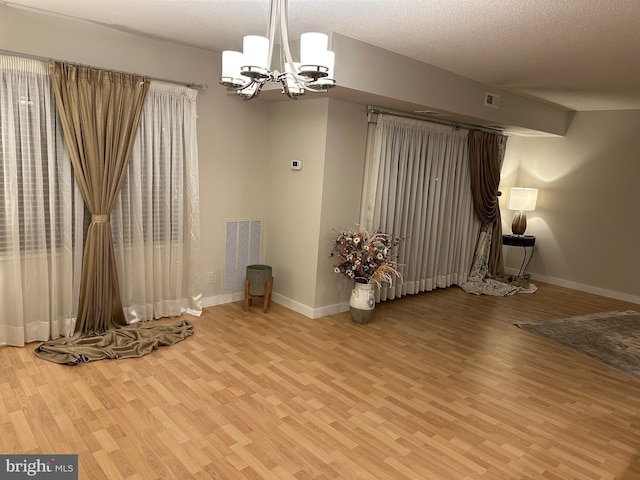 spare room with wood-type flooring, a chandelier, and a textured ceiling