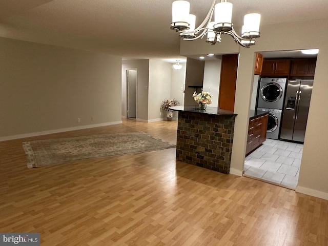 kitchen with pendant lighting, light hardwood / wood-style flooring, stacked washer and clothes dryer, stainless steel fridge with ice dispenser, and a chandelier