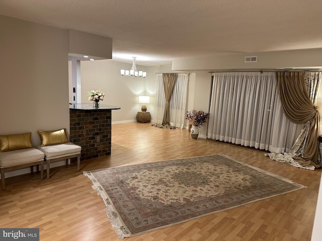 living area with a chandelier, a textured ceiling, and light wood-type flooring