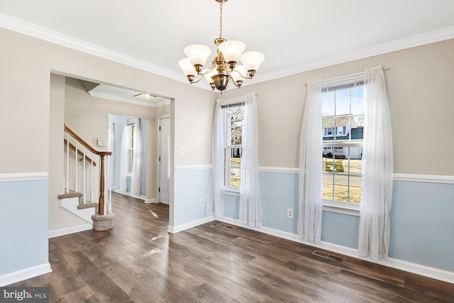 unfurnished dining area featuring dark wood-type flooring, crown molding, and an inviting chandelier