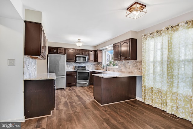 kitchen with appliances with stainless steel finishes, sink, backsplash, dark hardwood / wood-style floors, and dark brown cabinets