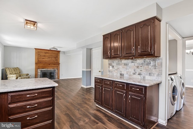 kitchen with a fireplace, dark hardwood / wood-style flooring, dark brown cabinets, tasteful backsplash, and washer and clothes dryer