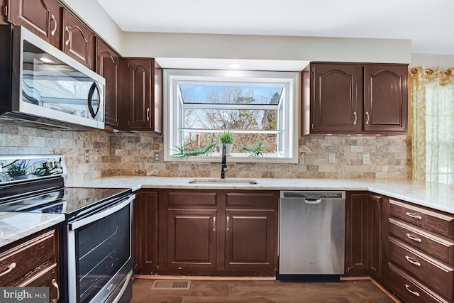 kitchen with sink, tasteful backsplash, light stone counters, appliances with stainless steel finishes, and dark hardwood / wood-style floors