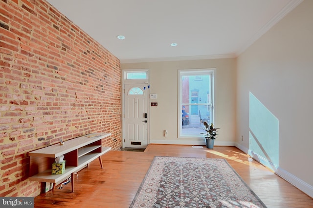 entryway featuring brick wall, crown molding, baseboards, and wood finished floors