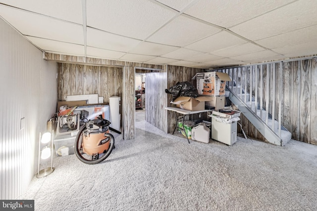 basement featuring wooden walls, a paneled ceiling, and carpet flooring