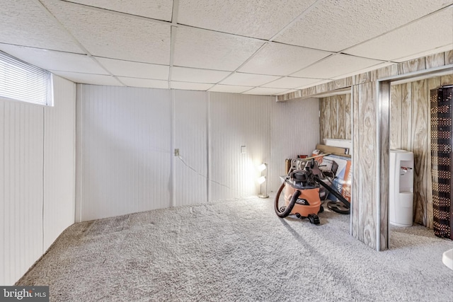 basement with a paneled ceiling, wooden walls, and carpet floors