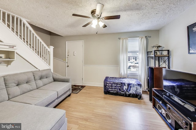 living room with a textured ceiling, ceiling fan, and light wood-type flooring