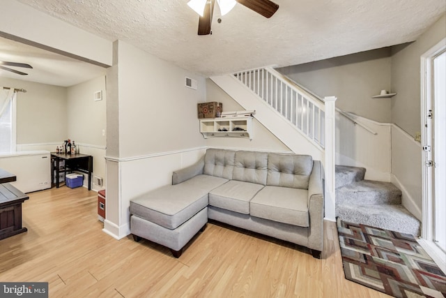 living room with ceiling fan, light hardwood / wood-style floors, and a textured ceiling