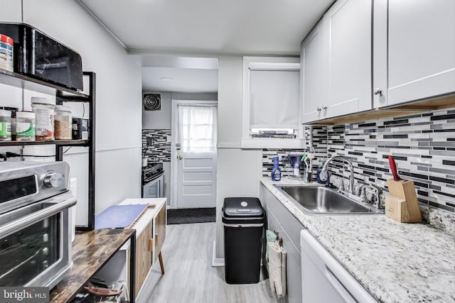 kitchen with sink, dishwasher, light hardwood / wood-style floors, light stone countertops, and white cabinets