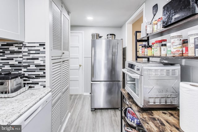 kitchen featuring tasteful backsplash, light stone counters, light hardwood / wood-style flooring, stainless steel refrigerator, and white cabinets