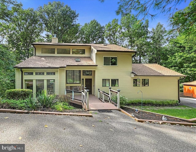 view of front of house featuring roof with shingles, a chimney, and a wooden deck