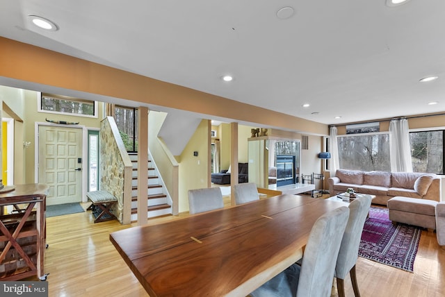 dining space featuring light wood-type flooring, a fireplace, recessed lighting, and stairs