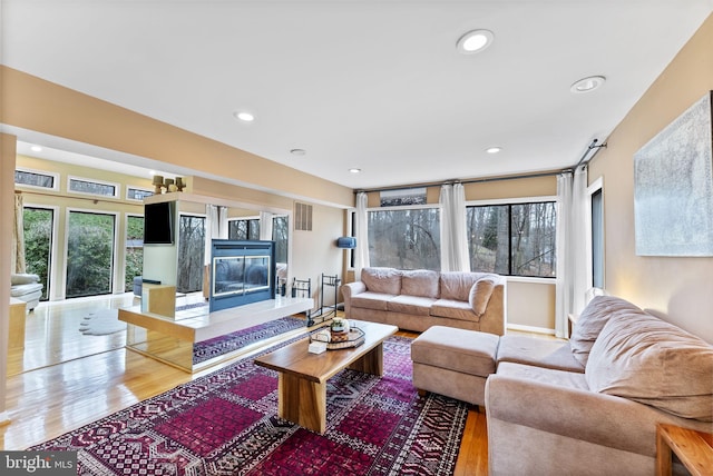 living area featuring recessed lighting, visible vents, a premium fireplace, and wood finished floors