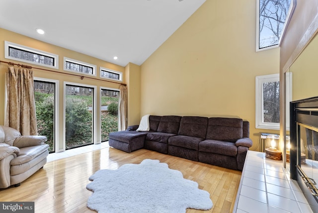 living area featuring high vaulted ceiling, a glass covered fireplace, recessed lighting, and wood finished floors