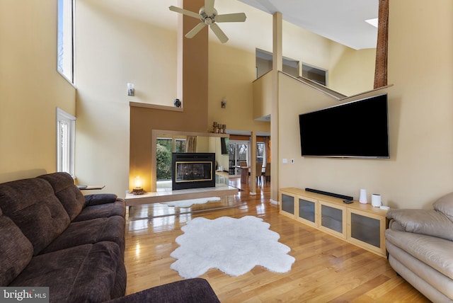 living area featuring lofted ceiling, a ceiling fan, wood finished floors, and a glass covered fireplace