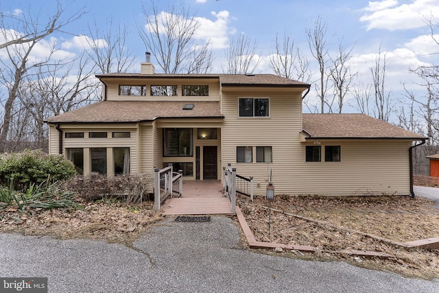 view of front facade with a shingled roof, a chimney, and a wooden deck