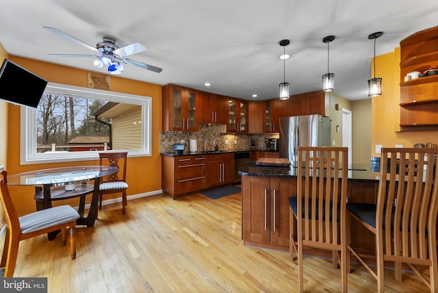 kitchen featuring stainless steel appliances, a sink, light wood-style floors, tasteful backsplash, and glass insert cabinets