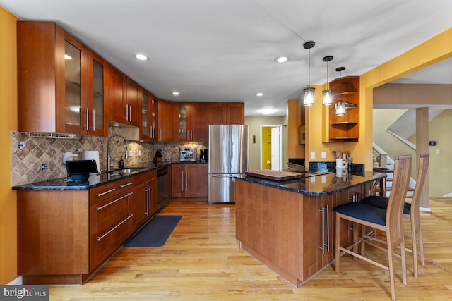 kitchen with stainless steel appliances, a sink, a peninsula, and light wood finished floors