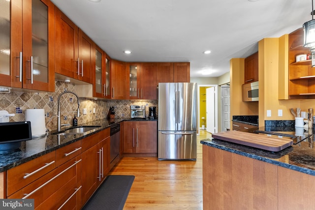 kitchen with light wood-type flooring, dark stone countertops, stainless steel appliances, and a sink