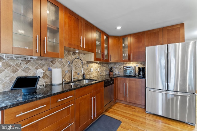 kitchen with brown cabinetry, glass insert cabinets, appliances with stainless steel finishes, light wood-style floors, and a sink