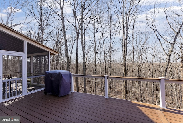 wooden terrace with grilling area, a sunroom, and a view of trees