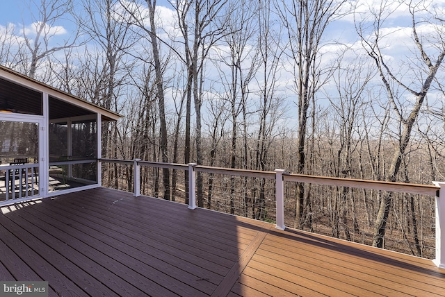 wooden terrace featuring a forest view and a sunroom