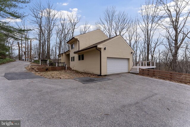 view of side of home with a garage, fence, a deck, and aphalt driveway