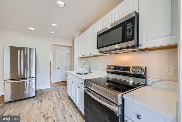 kitchen featuring sink, appliances with stainless steel finishes, white cabinetry, light stone countertops, and light wood-type flooring