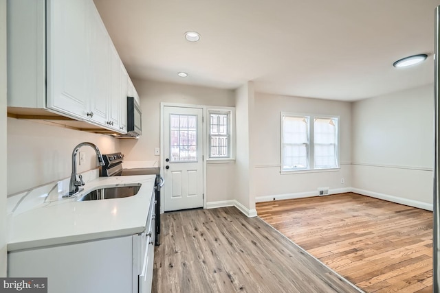 kitchen with sink, white cabinets, stainless steel range with electric stovetop, plenty of natural light, and light hardwood / wood-style flooring