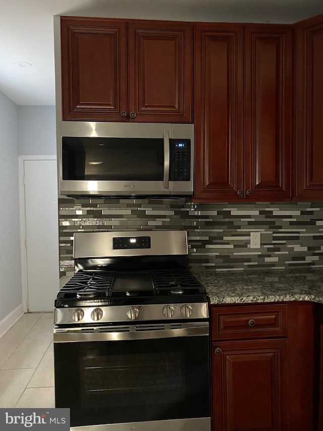 kitchen with dark stone countertops, backsplash, light tile patterned flooring, and appliances with stainless steel finishes