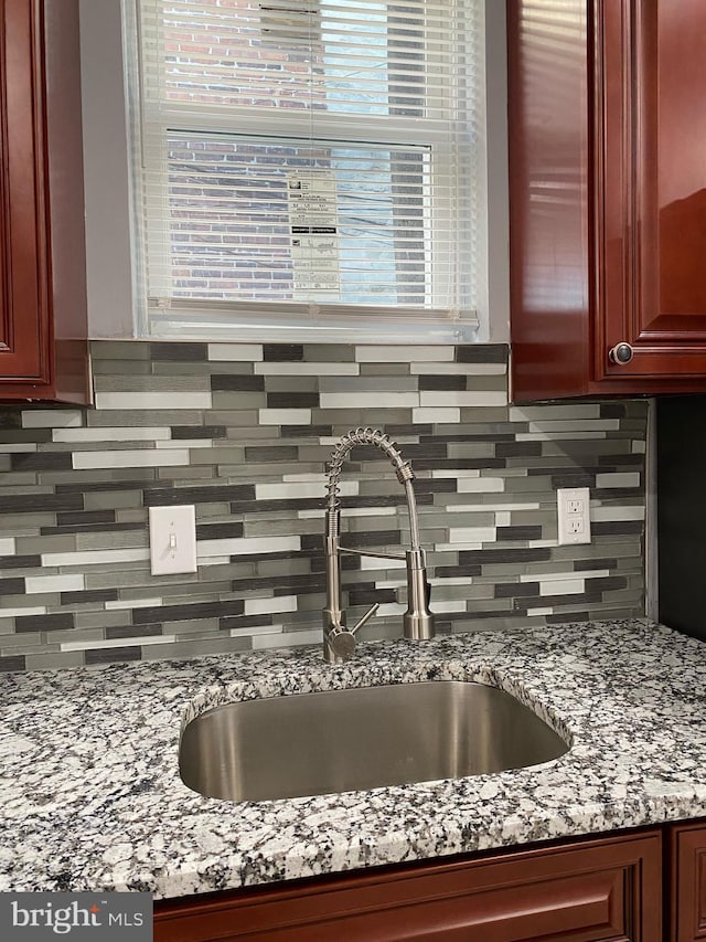 kitchen featuring light stone counters, sink, decorative backsplash, and a healthy amount of sunlight