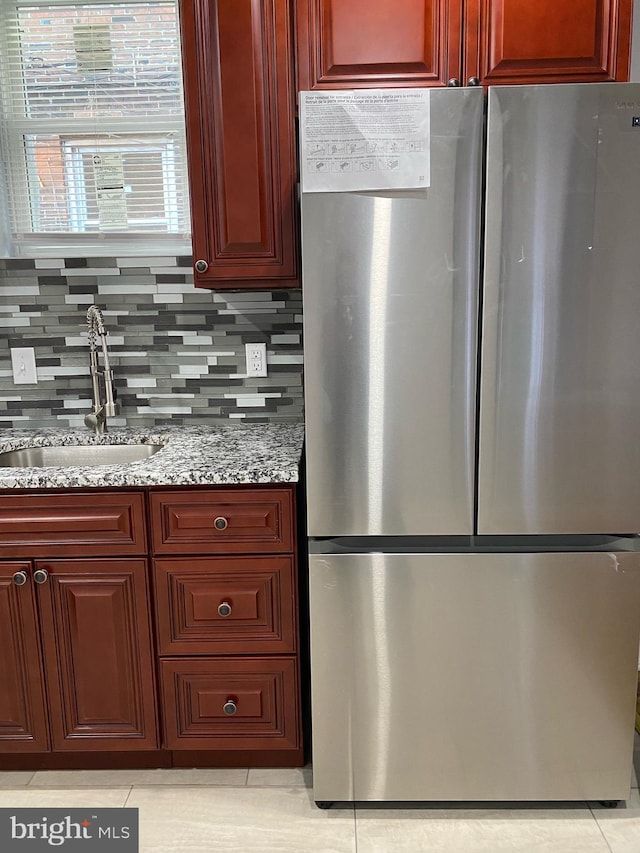 kitchen with sink, stainless steel refrigerator, tasteful backsplash, light stone countertops, and light tile patterned flooring