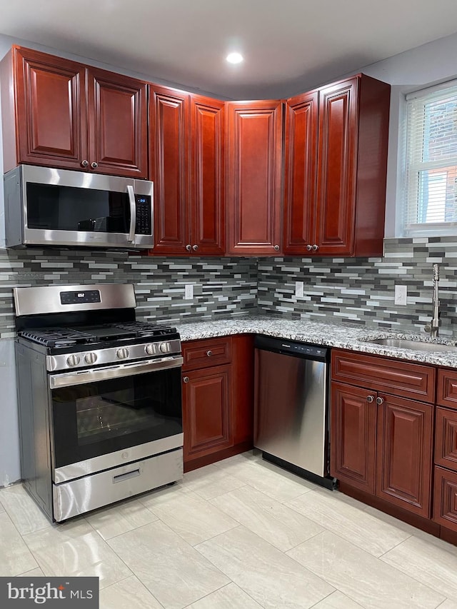 kitchen featuring light stone countertops, appliances with stainless steel finishes, sink, and backsplash