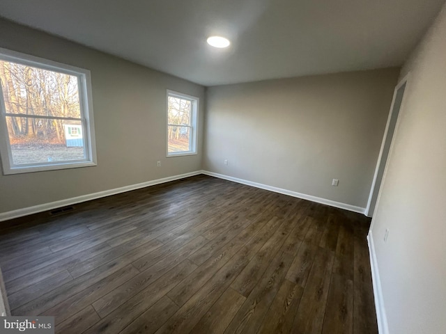 unfurnished room featuring visible vents, baseboards, and dark wood-type flooring