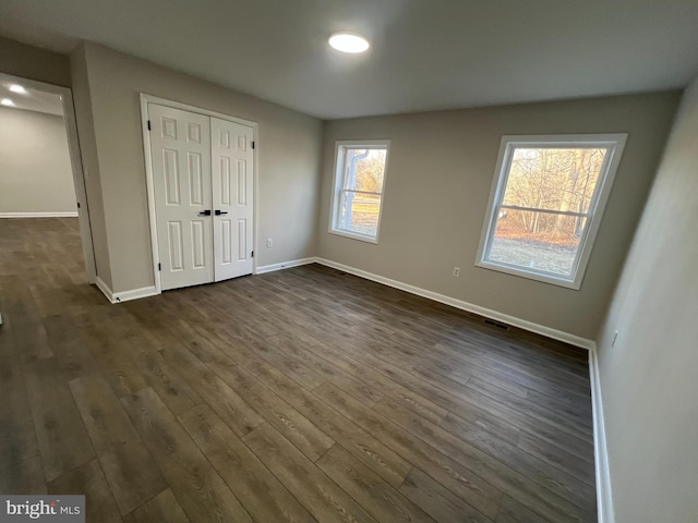 unfurnished bedroom featuring dark wood-type flooring, a closet, visible vents, and baseboards