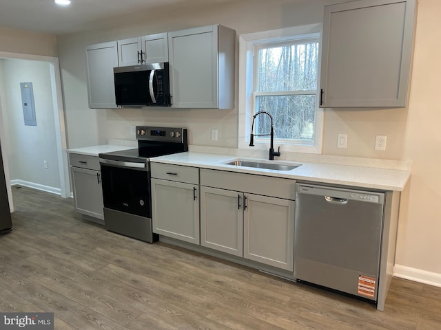 kitchen featuring light countertops, appliances with stainless steel finishes, light wood-style floors, a sink, and baseboards