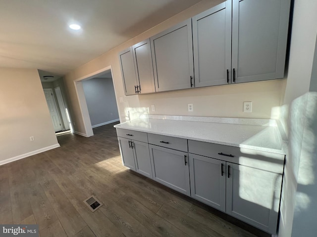 kitchen featuring baseboards, visible vents, dark wood-style flooring, light stone countertops, and gray cabinets