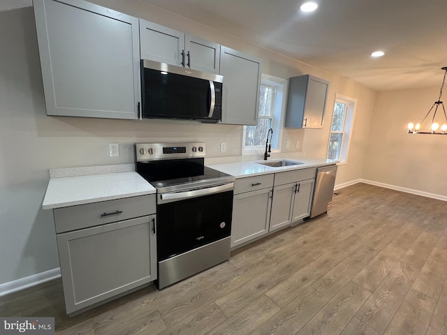 kitchen with light countertops, appliances with stainless steel finishes, a sink, and gray cabinetry