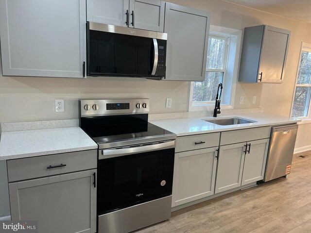 kitchen with light wood finished floors, light stone counters, appliances with stainless steel finishes, gray cabinets, and a sink