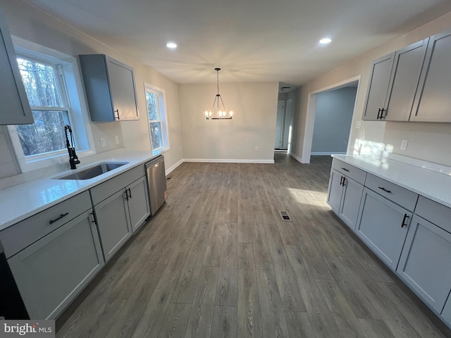 kitchen featuring pendant lighting, light countertops, gray cabinetry, a sink, and dishwasher