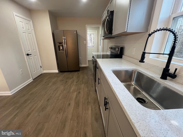 kitchen featuring appliances with stainless steel finishes, dark wood-style flooring, a sink, and light stone countertops