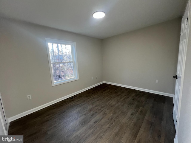 empty room with dark wood-style floors, visible vents, and baseboards