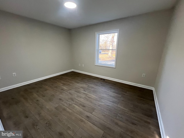 unfurnished room featuring dark wood finished floors, visible vents, and baseboards