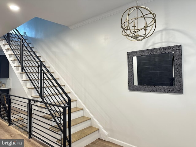 stairway with crown molding, hardwood / wood-style floors, and a chandelier